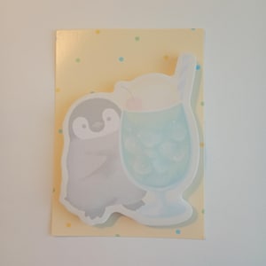 Puede incluir: Una ilustración caprichosa presenta un pingüino gris junto a una bebida azul con hielo y una cereza. La imagen está sobre un fondo amarillo con pequeños lunares de colores. El pingüino y la bebida son formas recortadas.