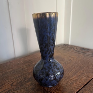 May include: A small, blue vase with a speckled pattern and a gold rim. The vase has a bulbous base and a flared neck. It is sitting on a wooden surface.