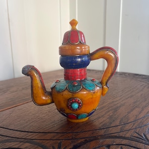 May include: A decorative teapot with a vibrant color scheme. The teapot features a yellow body, a red and orange lid, and a blue and red neck. It is adorned with turquoise and red accents, and has a curved handle and spout.
