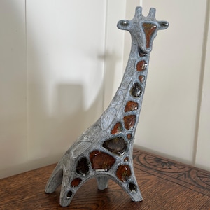 May include: A decorative giraffe figurine with a gray and brown mosaic design. The giraffe has a long neck and is standing on four legs. The figurine is made of a stone-like material and is displayed on a wooden surface.