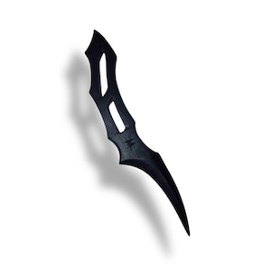 May include: A black dagger with a curved blade and a decorative handle. The handle has cut-out designs and a small star-like symbol. The dagger is set against a white background, casting a shadow.
