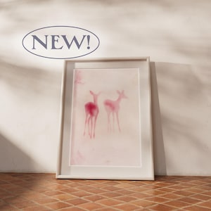 May include: A framed rectangular wall art print featuring two watercolour-style deer silhouettes in shades of pink and magenta against a pale, off-white background. The text NEW! is displayed in a dark blue oval above the frame.