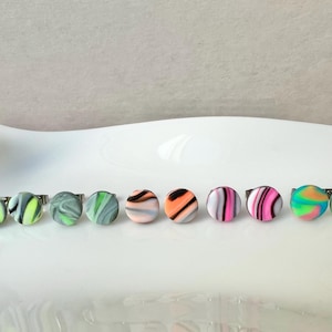 Könnte beinhalten: Ein Set mit acht bunten, runden Ohrringen mit Wirbelmustern. Die Ohrringe sind aus Polymer Clay gefertigt und haben eine silberne Rückseite.