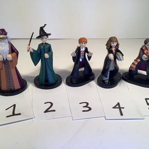 Puede incluir: Cinco figuras de personajes de Harry Potter, incluyendo Dumbledore, Hermione, Ron, Harry y Snape. Las figuras están en varias posturas y están hechas de plástico. Se muestran en una superficie blanca con los números del 1 al 5 debajo de cada figura.