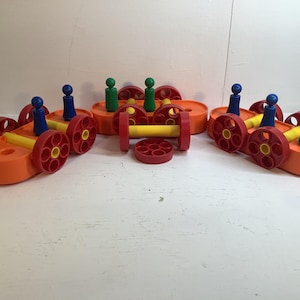 Könnte beinhalten: Eine Sammlung farbenfroher Spielzeugfahrzeuge aus Kunststoff. Jedes Fahrzeug ist orange mit roten Rädern und gelben Verbindungsstangen. Blaue und grüne Spielfiguren befinden sich oben auf den Fahrzeugen. Ein lustiges, lehrreiches Spielzeug für Kinder.