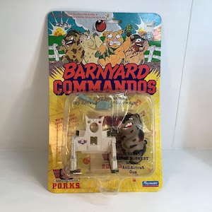 Peut inclure: Un ensemble de figurines d'action vintage Barnyard Commandos, avec un personnage de cochon et un canon anti-aérien. L'emballage est jaune et bleu, avec des illustrations de cochons et le texte "Barnyard Commandos".
