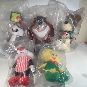 May include: Five plush toys of cartoon characters, each sealed in a clear plastic bag. The characters include a gray and white skunk, a brown Tasmanian Devil, a white dog, a red and white striped cat, and a yellow Tweety Bird.