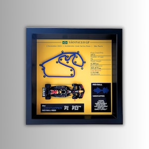 Peut inclure: Tableau encadré représentant une voiture de course de Formule 1 et le tracé du circuit. L'image comprend le texte "SÃO PAULO GP" et des détails sur la course, dont une longueur de piste de 4,309 km. L'œuvre est dans un cadre noir.