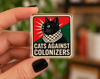 May include: A square pin featuring a black cat wearing a keffiyeh pattern scarf. The background is divided diagonally into red and green sections with a white sunburst design. The text CATS AGAINST COLONIZERS is printed in black at the bottom.