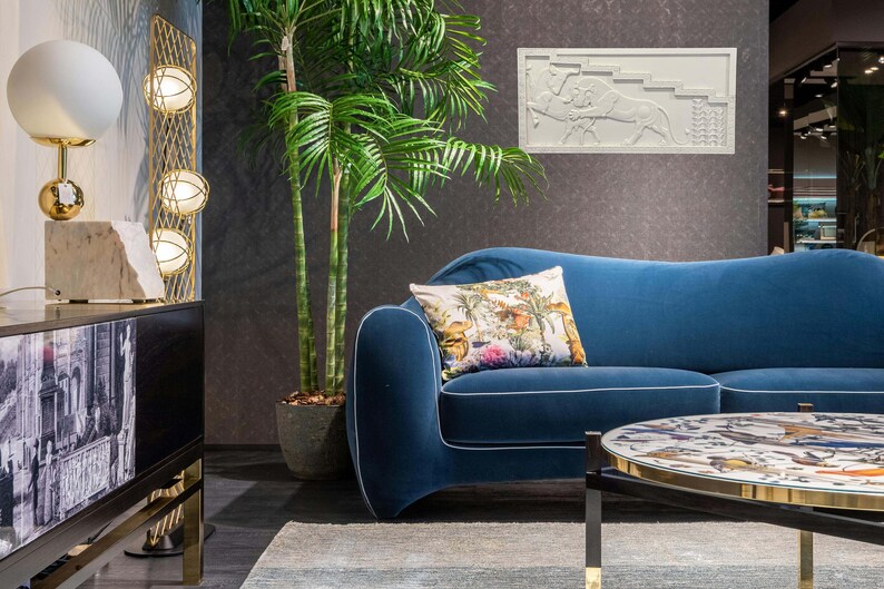 May include: A blue velvet sofa with a floral patterned pillow, a gold metal floor lamp with three white globe lights, and a round coffee table with a patterned top.