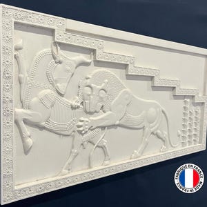May include: White plaster relief sculpture of a lion attacking a bull. The sculpture is framed by a decorative border of small flowers. The sculpture is made in France.