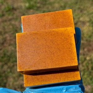 Puede incluir: Dos barras de jabón de color naranja apiladas una encima de la otra. El jabón tiene una textura granulada.