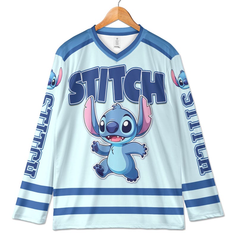 Puede incluir: Camiseta de hockey azul claro con la palabra "STITCH" en letras azules grandes y un personaje de dibujos animados. La camiseta tiene rayas azules y la palabra "STITCH" verticalmente en las mangas. La camiseta est&aacute; colgada en una percha de madera.