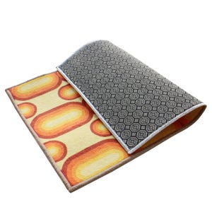 May include: A yellow, orange, and black patterned rug with a geometric design on the back. The rug is folded in half and the back is visible.