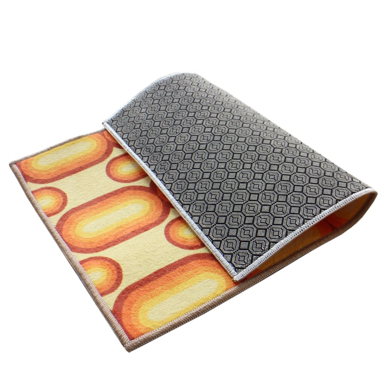 May include: A yellow, orange, and black patterned rug with a geometric design on the back. The rug is folded in half and the back is visible.