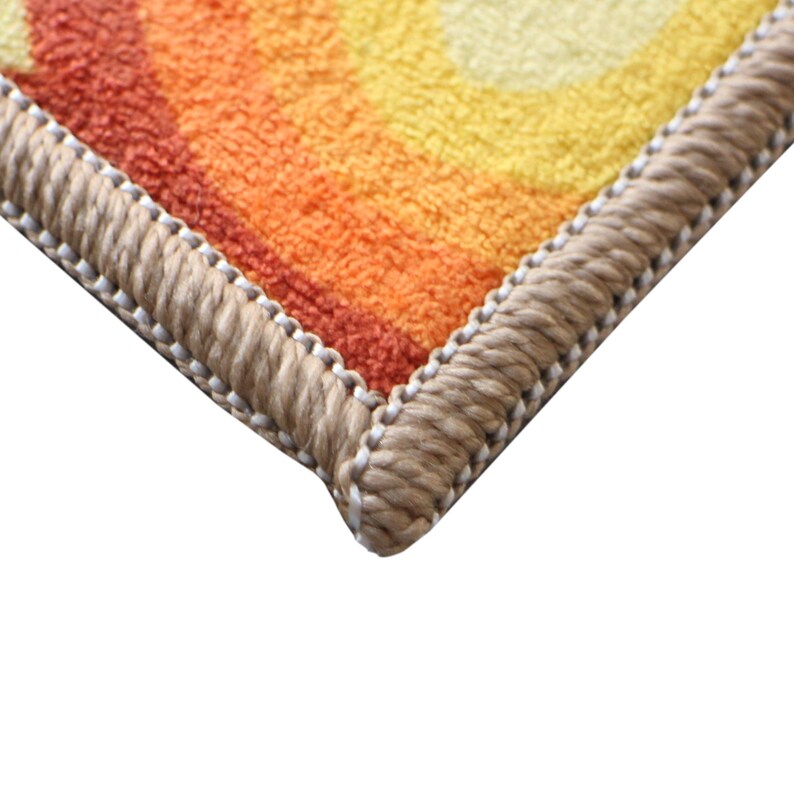 May include: Close-up of the edge of a colorful rug with a woven border. The rug has a pattern of orange, yellow, and red stripes.