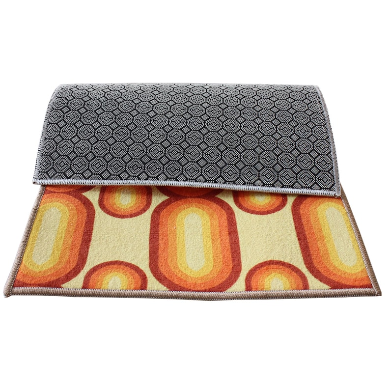 May include: A reversible rug with a geometric pattern on one side and a retro, abstract design on the other side. The geometric side is black and white, while the abstract side features orange, yellow, and white.