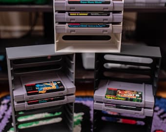 Puede incluir: Tres soportes para cartuchos de juegos impresos en 3D, cada uno con varios cartuchos de juegos de Super Nintendo Entertainment System (SNES). Los juegos incluyen "Super Mario World", "Mario is Missing!" y "The Legend of Zelda: A Link to the Past".