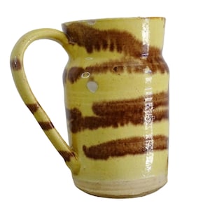 Op de afbeelding: Een gele keramische mok met bruine strepen. De mok heeft een handvat en is geglazuurd.