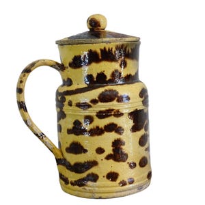 May include: A brown and yellow ceramic jug with a lid. The jug has a brown and yellow mottled glaze with a brown handle.