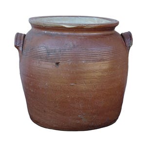 Op de afbeelding: Een bruine keramische pot met twee handvatten, een brede opening en een lichtgekleurde binnenkant. De pot heeft horizontale lijnen in het midden. Een rustiek, vintage stuk, tegen een witte achtergrond.