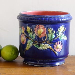 May include: A cobalt blue ceramic planter with a floral design in pink, yellow, and green. The planter has a pink interior and sits on a wooden surface. Limes are in the foreground.