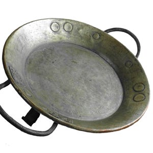 Könnte beinhalten: Eine antike Kupferpfanne mit zwei schwarzen Metallgriffen. Die Pfanne hat eine abgenutzte, grüne Patina und ist leicht oval.