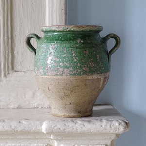 Op de afbeelding: Een tweekleurige keramische pot met een felgroen geglazuurd bovengedeelte met zichtbare slijtage en een natuurlijk, ongeglazuurd beige onderlichaam. De pot heeft een brede, afgeronde rand en twee symmetrische handvatten aan de zijkanten.
