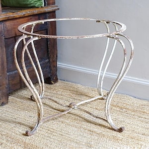 May include: An antique, white metal plant stand with an oval top and curved legs. The stand has a distressed, aged appearance with visible rust and wear. The stand is approximately 61 cm tall.