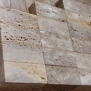 May include: A wall made of light gray and beige stone tiles with a rough, textured surface.