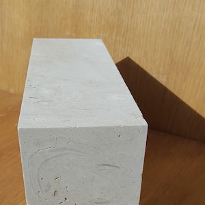 May include: A white rectangular block of concrete with a smooth surface and subtle marbling. The block is sitting on a wooden surface.