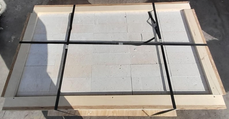 May include: A white ceramic tile sheet secured with black straps in a wooden crate.