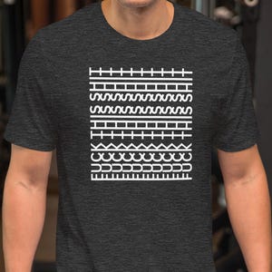 以下が含まれることがあります： 白の幾何学模様が施された濃い灰色のTシャツ。 デザインは、直線、波、ジグザグなど、さまざまなパターンを持つ一連の水平線が特徴です。 半袖のシャツは柔らかい素材で作られているようです。