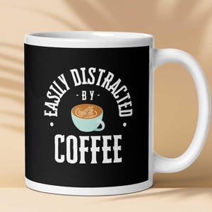 May include: White ceramic mug with a black design that says "Easily Distracted - By - Coffee" with a cartoon image of a cup of coffee.