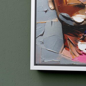May include: Abstract painting of a face with bold strokes of red, pink, white, and blue paint. The painting is framed in a white frame.