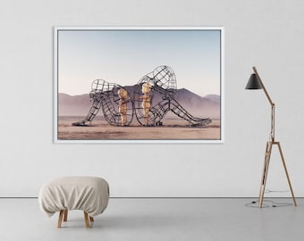May include: A framed photograph of a metal sculpture of three figures in a desert landscape. The figures are made of wire and are arranged in a way that suggests they are embracing. The sculpture is set against a backdrop of a vast, empty desert.