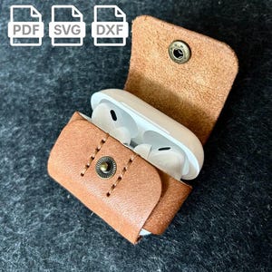 May include: A tan leather case with a press stud closure, containing white wireless earbuds. The case is open, displaying the earbuds. The image also includes PDF, SVG, and DXF file icons.