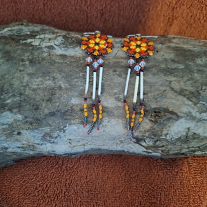 May include: A pair of beaded earrings with a geometric pattern in orange, yellow, and black. The earrings have a crystal bead and a white feather dangle.