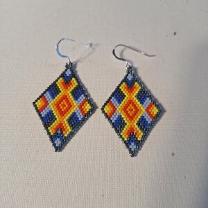 May include: A pair of diamond-shaped earrings with a geometric pattern in shades of blue, yellow, orange, and black.