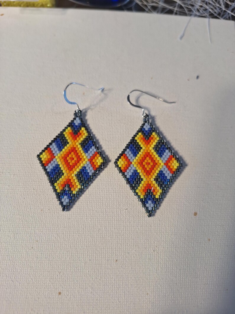 May include: A pair of diamond-shaped earrings with a geometric pattern in shades of blue, yellow, orange, and black.