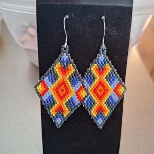 May include: A pair of beaded earrings with a geometric design in shades of blue, yellow, orange, and black.