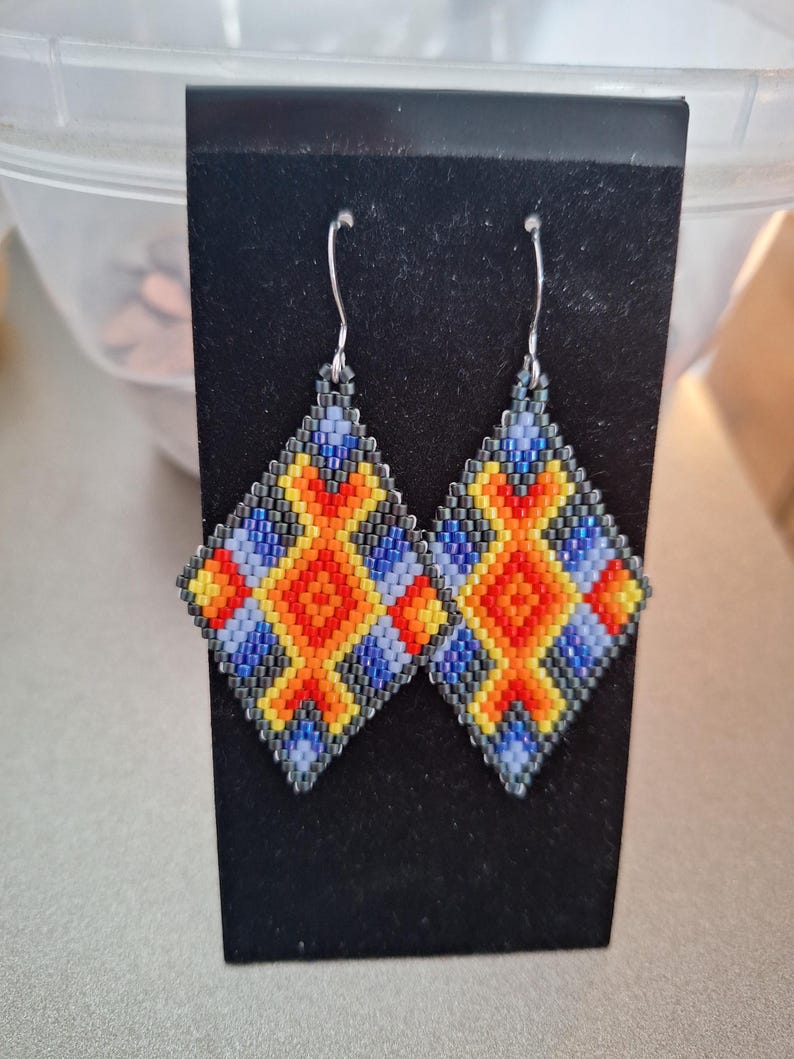 May include: A pair of beaded earrings with a geometric design in shades of blue, yellow, orange, and black.