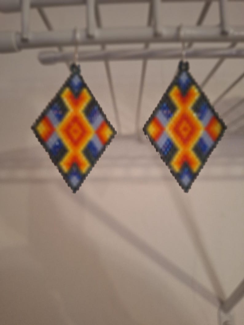 May include: A pair of diamond-shaped earrings with a geometric pattern in shades of blue, orange, yellow, and black.