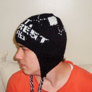 May include: Black knit hat with ear flaps and white text. The hat has a geometric pattern and the text "FIRE" is visible. The hat has braided black and white ties.