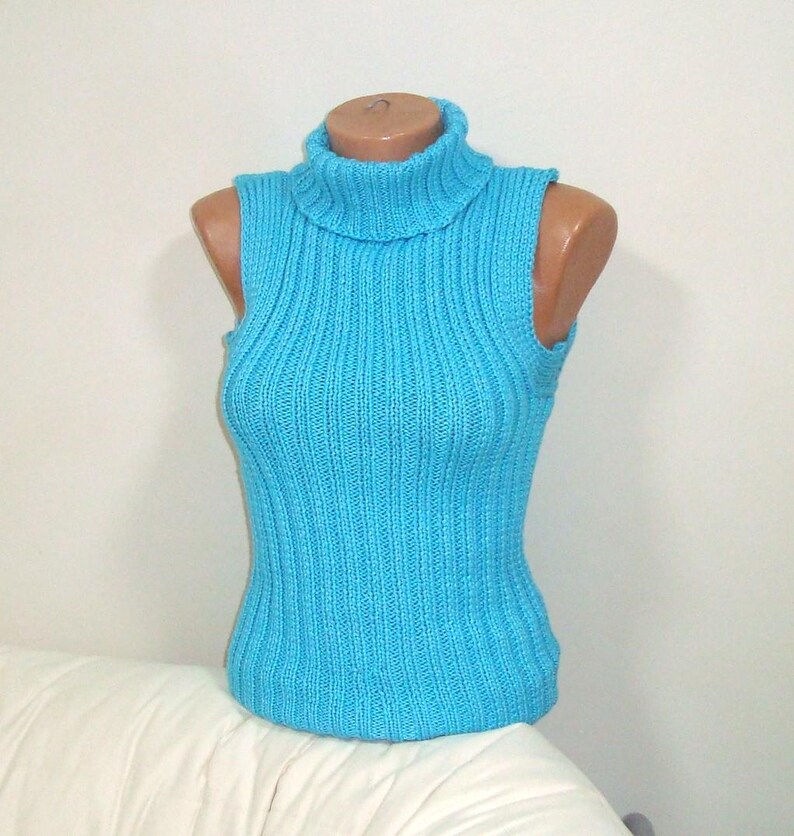 May include: A sleeveless, turquoise blue turtleneck sweater displayed on a mannequin. The ribbed knit top has a high, folded collar and a fitted silhouette. The sweater is made of a soft, possibly wool or cotton blend.