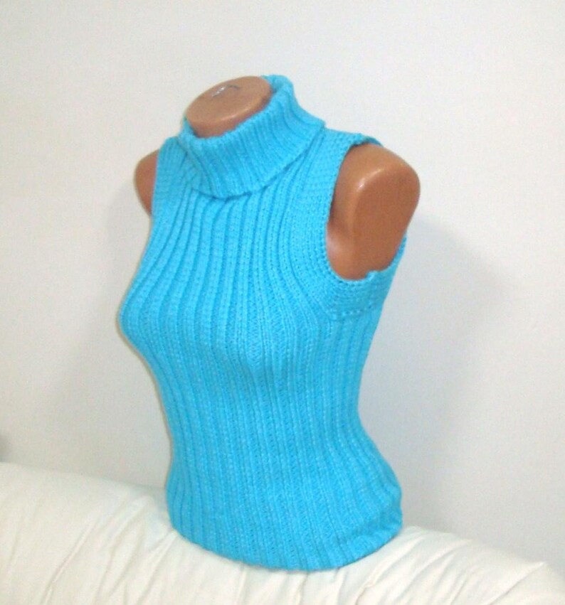 May include: A sleeveless, turquoise blue ribbed knit top with a turtleneck collar. The top is displayed on a mannequin and has a form-fitting silhouette. The knitwear has vertical ribbing and a high neckline.