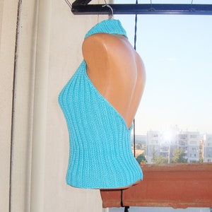 May include: A turquoise halter top made of knitted fabric. The top features a ribbed texture and a high neckline that transitions into a halter design. The back is open, and the top is displayed on a mannequin.