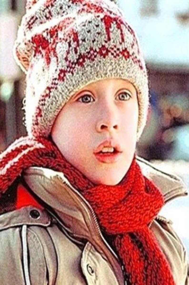 May include: A person wearing a red and white patterned knitted hat and a red scarf. They are also wearing a tan jacket with a zip. The image is a medium shot, focusing on the person's face and upper body.
