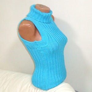 May include: A sleeveless, turquoise blue knitted turtleneck top. The top is displayed on a mannequin, showcasing its ribbed texture and form-fitting design. The turtleneck is folded over, and the armholes are open.