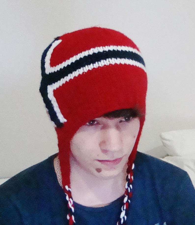 May include: A red knitted hat with a white and black striped design. The hat has a long, dangling tassel.